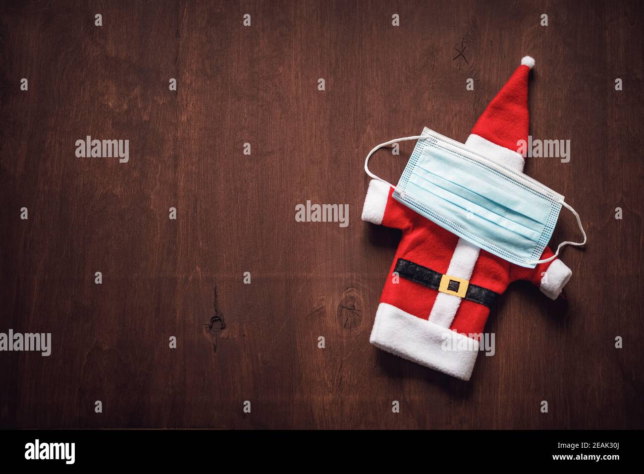 Weihnachtsmann Kleidung mit einer medizinischen Gesichtsmaske auf braunem Holz Hintergrund Stockfoto