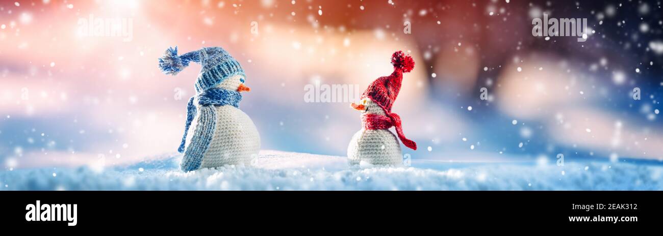 Kleine gestrickte Schneemänner auf weichem Schnee auf blauem Hintergrund Stockfoto