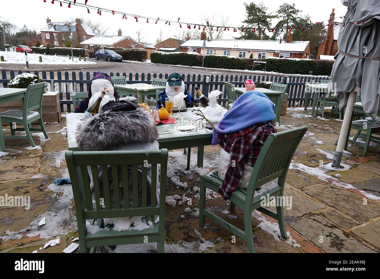 Ashford, Kent, Großbritannien. 10. Februar 2021. Aufgrund der Pandemie musste das Chequers on the Green Pub an der Ashford Rd A28 in High Halden schließen und hat eine neuartige Möglichkeit entwickelt, Passanten mit Schnee zu amüsieren, der von Storm Darcy kommt. Eine Familie von Schneefiguren sitzt draußen, trinkt und isst. Foto-Kredit: Paul Lawrenson/Alamy Live Nachrichten Stockfoto