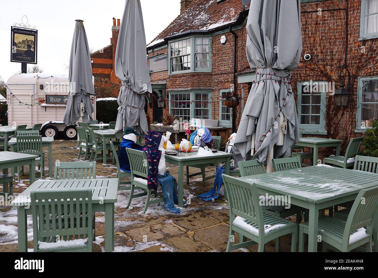Ashford, Kent, Großbritannien. 10. Februar 2021. Aufgrund der Pandemie musste das Chequers on the Green Pub an der Ashford Rd A28 in High Halden schließen und hat eine neuartige Möglichkeit entwickelt, Passanten mit Schnee zu amüsieren, der von Storm Darcy kommt. Eine Familie von Schneefiguren sitzt draußen, trinkt und isst. Foto-Kredit: Paul Lawrenson/Alamy Live Nachrichten Stockfoto