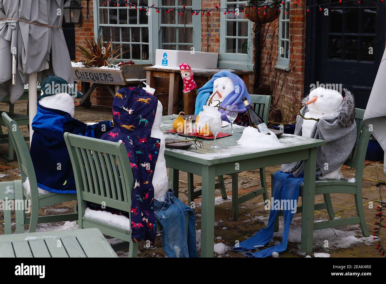 Ashford, Kent, Großbritannien. 10. Februar 2021. Aufgrund der Pandemie musste das Chequers on the Green Pub an der Ashford Rd A28 in High Halden schließen und hat eine neuartige Möglichkeit entwickelt, Passanten mit Schnee zu amüsieren, der von Storm Darcy kommt. Eine Familie von Schneefiguren sitzt draußen, trinkt und isst. Foto-Kredit: Paul Lawrenson/Alamy Live Nachrichten Stockfoto