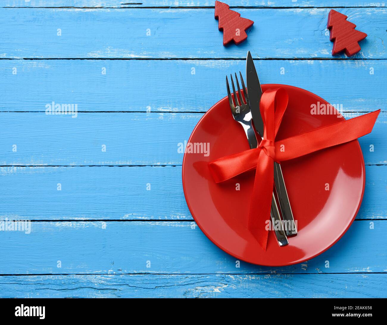 Runde Platte und Metall Gabel und Messer mit einem roten Seidenband gebunden, blauer Holzhintergrund Stockfoto