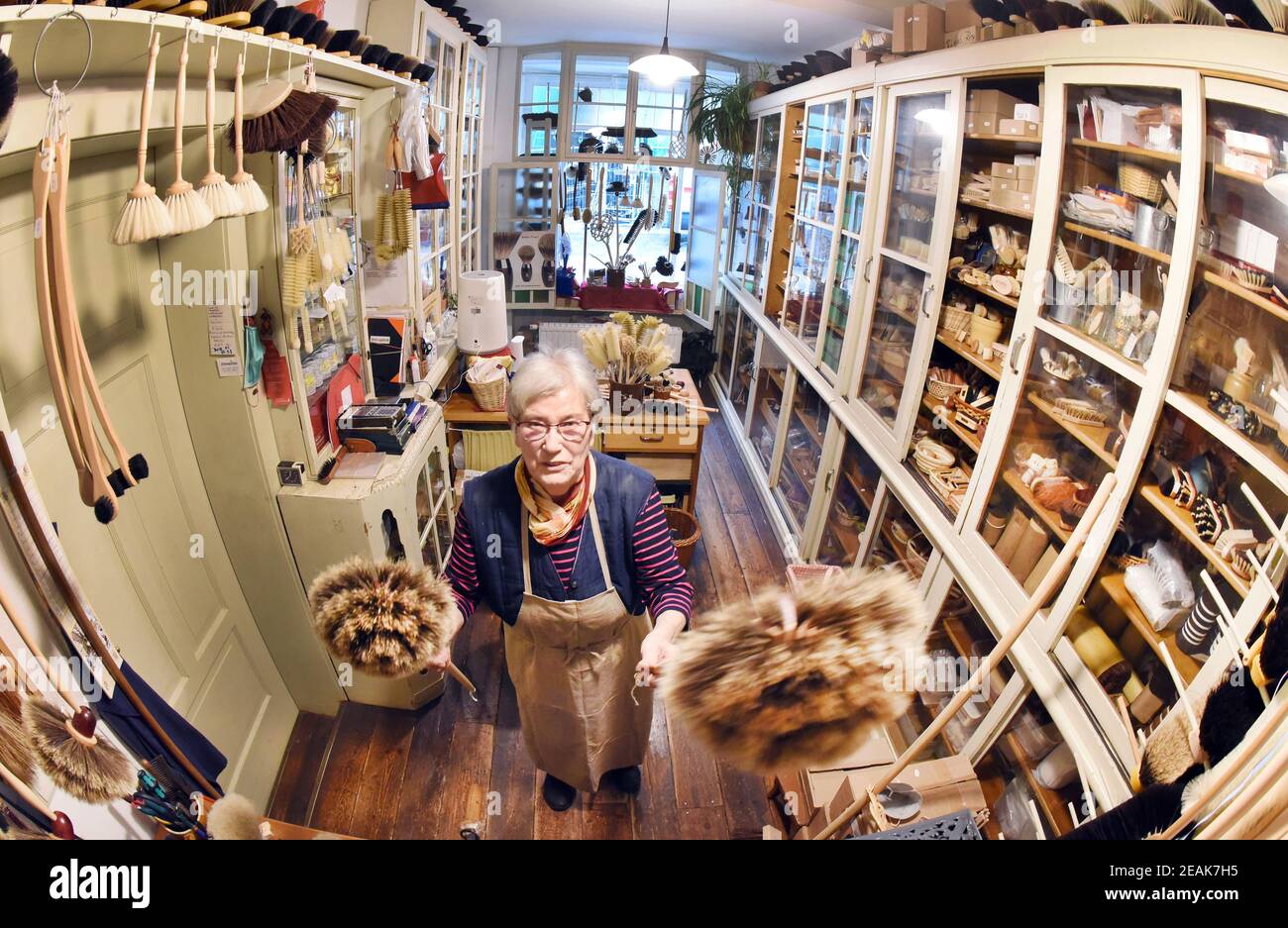 08. Februar 2021, Sachsen-Anhalt, Naumburg: In ihrer kleinen Bürstenmanufaktur, die auch als Verkaufsraum dient, hält die 81-jährige Bürstenmanufaktur Ursula Römer zwei Federstauber in den Händen. Obwohl ihr Laden wegen der Pandemie geschlossen ist, kommen derzeit viele Bestellungen aus ganz Deutschland per Telefon oder schriftlich für große und kleine Besen, Spinnenfeger, Federstauber oder sogar Wand- und Deckenbesen. In ihrem traditionellen Laden, den ihr Urgroßvater 1885 eröffnete, stellt die 81-Jährige ihre Pinsel und Besen mit einer Vielzahl von Borsten auf alte, traditionelle Weise mit der Hand her Stockfoto