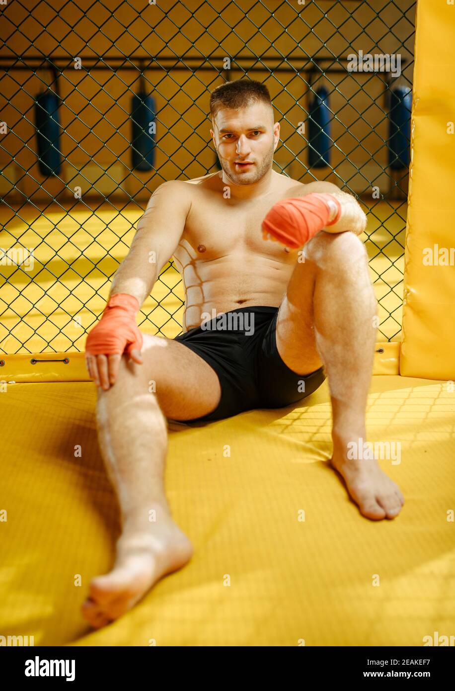 Männlicher MMA-Kämpfer, der in einem Käfig auf dem Boden sitzt Stockfoto