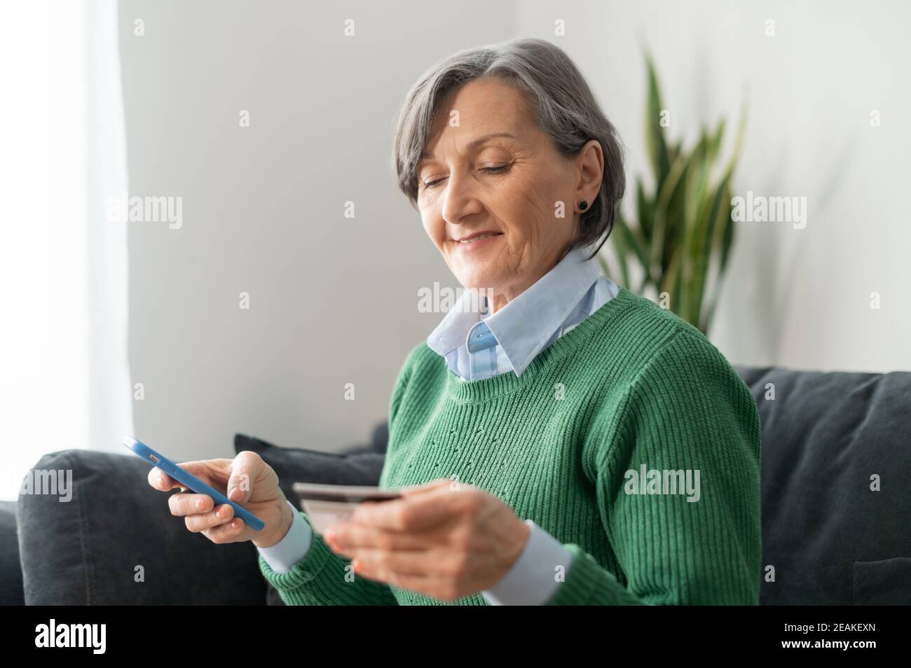 Ältere reife Geschäftsfrau hält ein Handy und Überprüfung Klärung Kreditkartennummer Online-Transaktion zu machen, ist die grauhaarige Großmutter Stockfoto