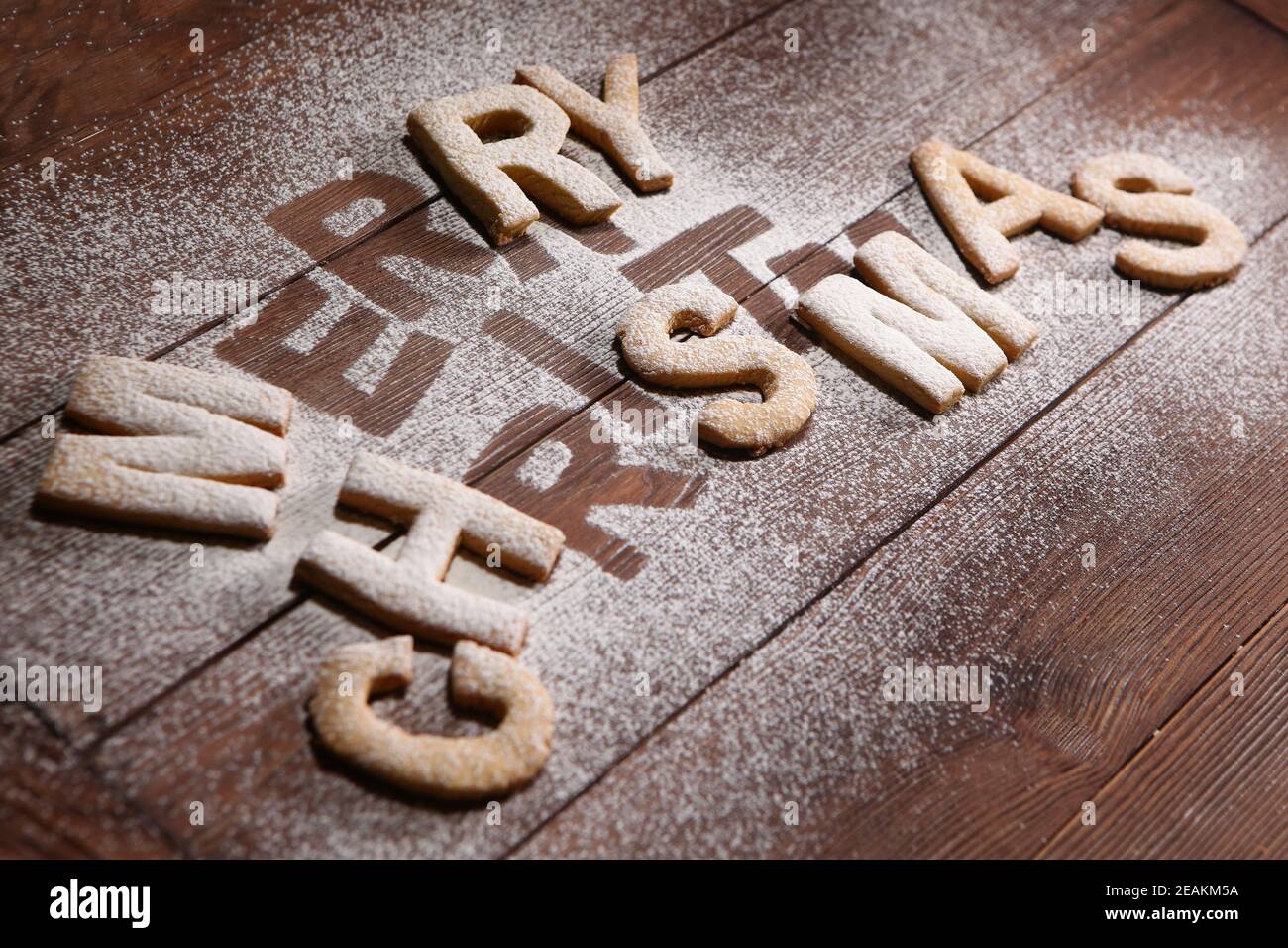 Die Inschrift fröhliche Weihnachts-Kekse in Form von Buchstaben aus Ingwerteig. Ingwerkeks. Handarbeit. Drucken Sie auf einem Holzhintergrund. Das Konzept der Feier. Weihnachten oder Neujahr. Stockfoto