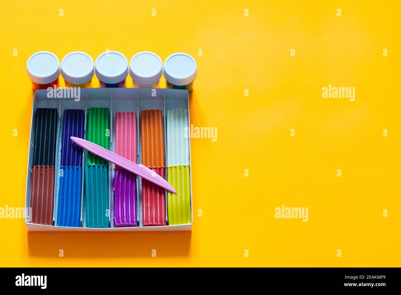 Auf gelbem Grund liegt eine Schachtel mit Plastilin und Farbe Stockfoto