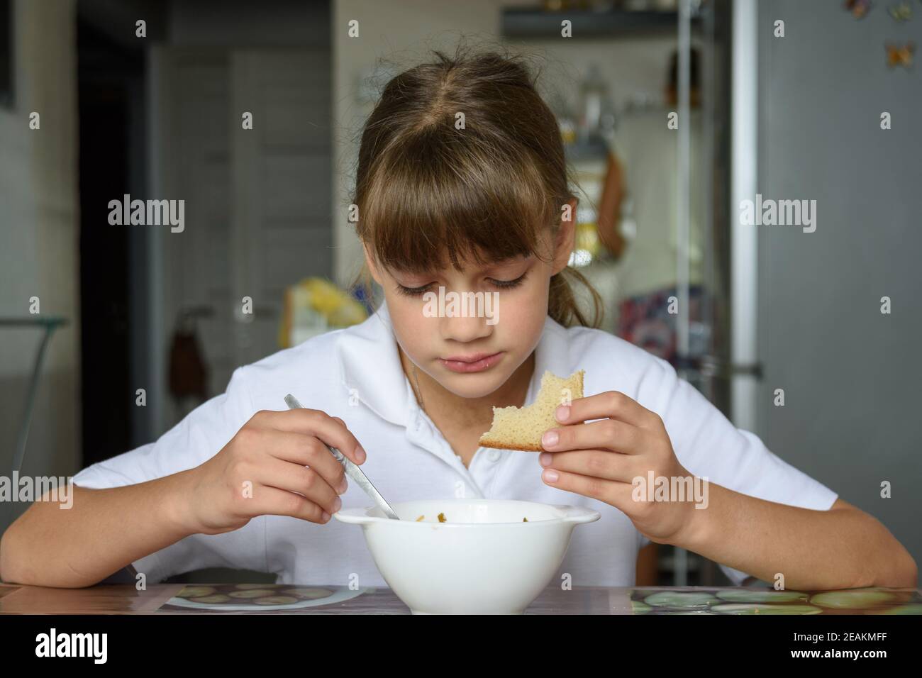 Ein Schulmädchen kam von der Schule und setzte sich zum Essen Am Tisch in der Küche zu Hause Stockfoto