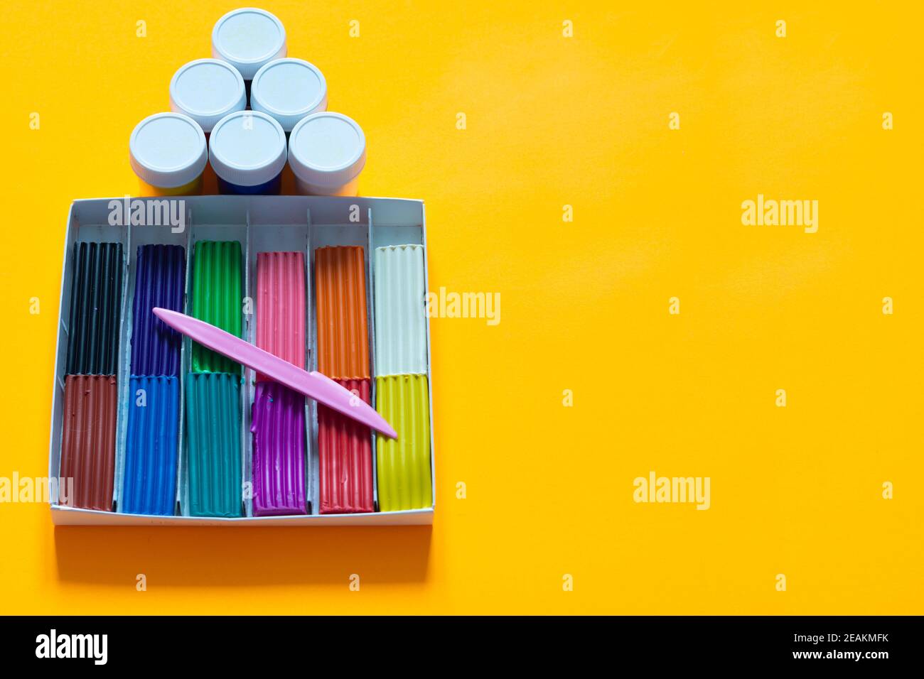 Über der Plastilin-Box befinden sich Gouachegefäße, gelber Hintergrund Stockfoto