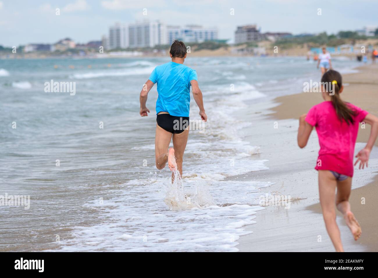 Ein Mann rennt am Strand entlang, ein Mädchen rennt ihm hinterher, Rückansicht Stockfoto