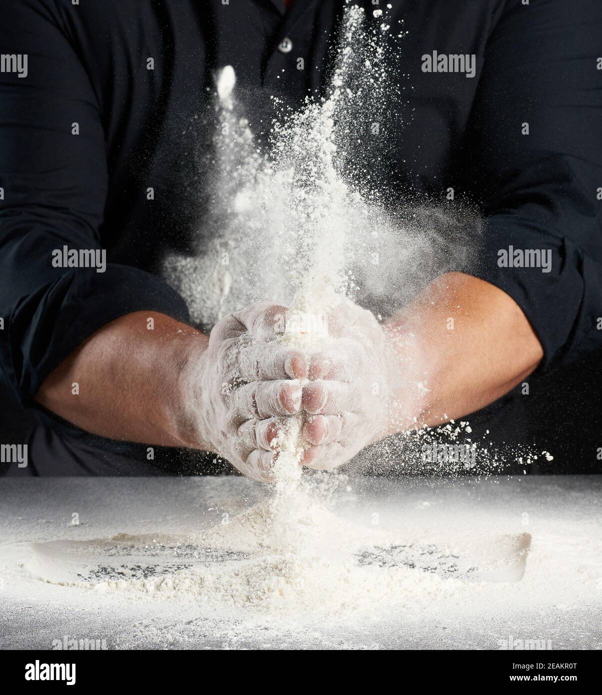 Mann in schwarzer Uniform streut Weizenmehl in verschiedenen Anweisungen Stockfoto