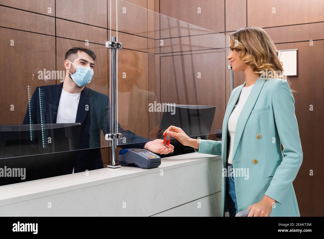 Hotelmanager in medizinischer Maske, der jungen Frau den Schlüssel gibt In der Lobby Stockfoto