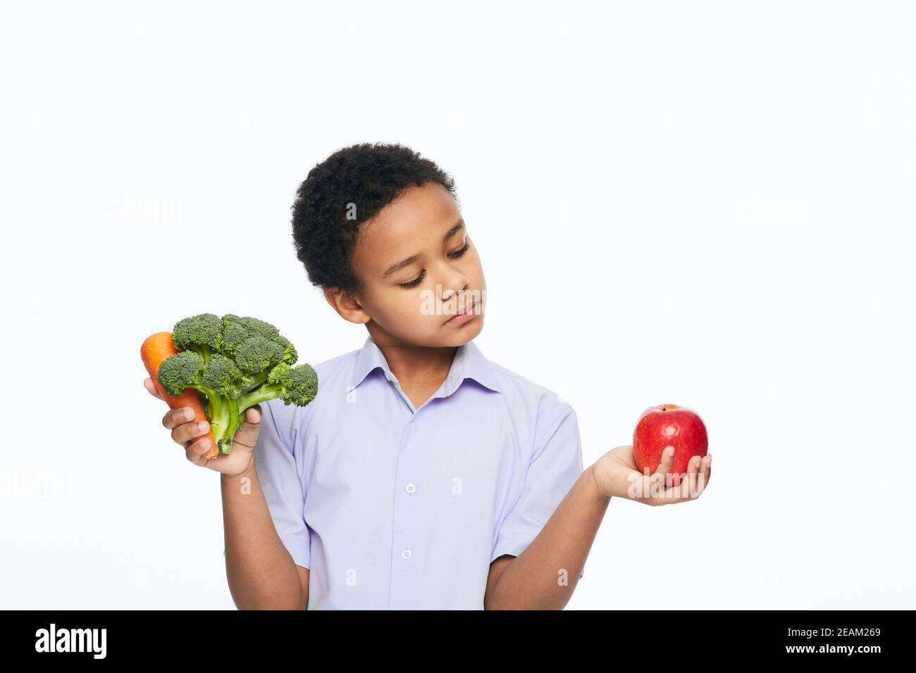 Der afroamerikanische Junge hält Karotten, Brokkoli und Apfel in der Hand. Gesund essen für Kinder Stockfoto