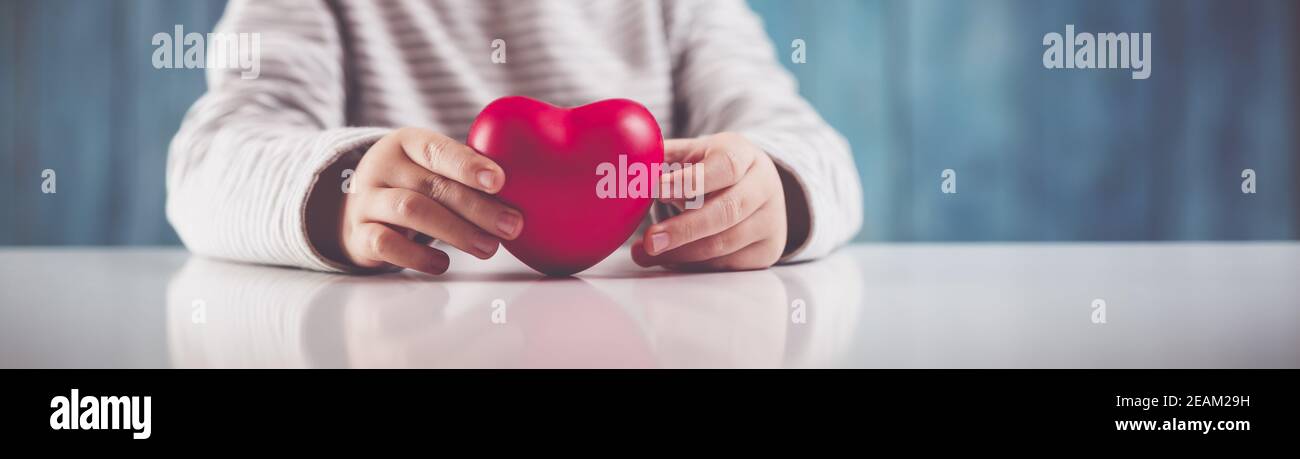 Süßes kleines Kind, das rotes Herz in den Händen hält Stockfoto