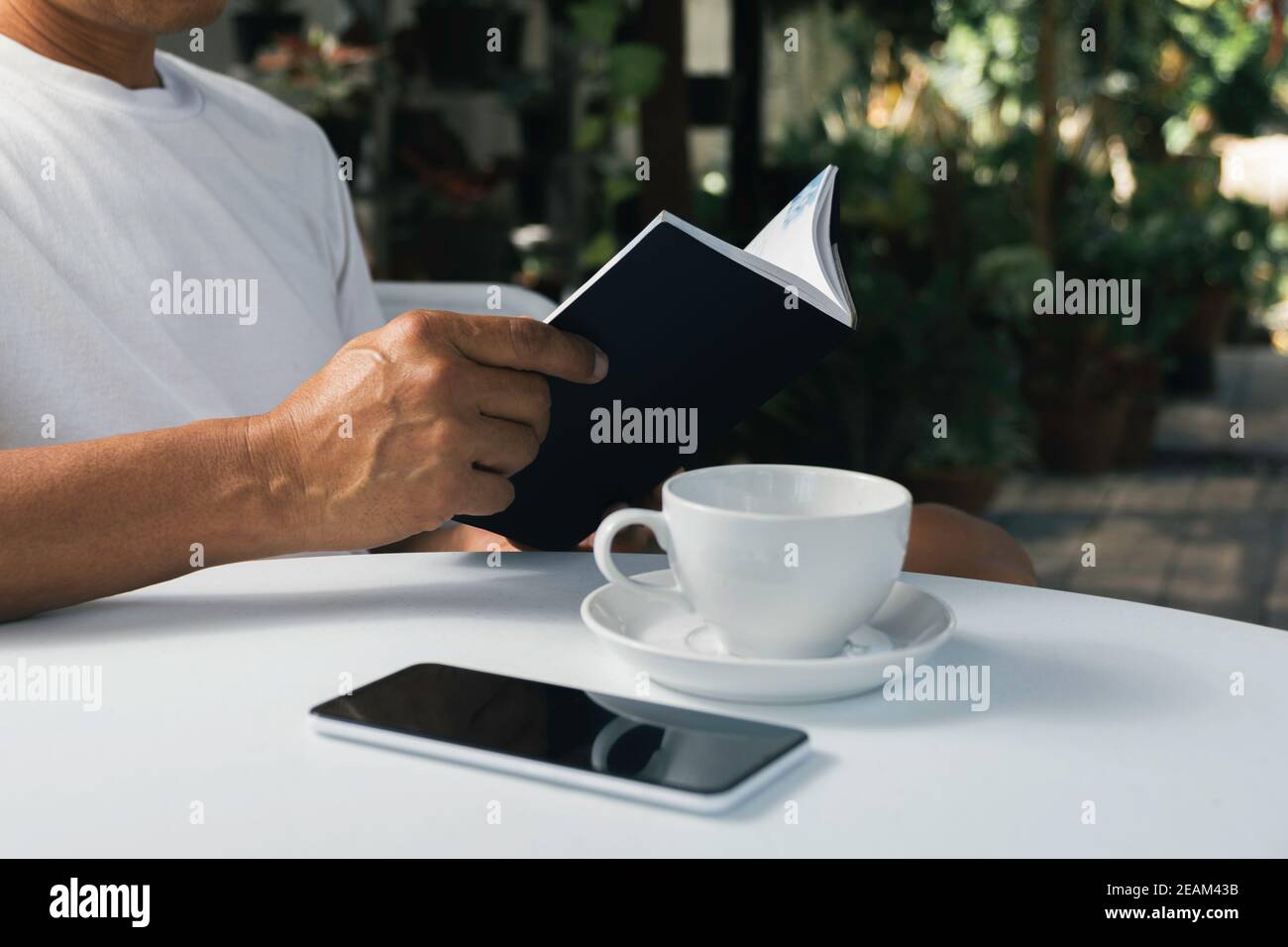 Ein Mann liest ein Buch mit Kaffeetasse. Mann sitzt im Stuhl zu Hause, Buch lesen und entspannen. Stockfoto