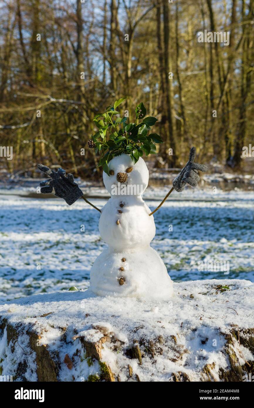 Niedlicher Schneemann aus drei Schneebällen mit Blättern für Haare, Zweige für Arme mit Kinderhandschuhen, Tannenzapfen für Nase und Steine für Knöpfe. Stockfoto