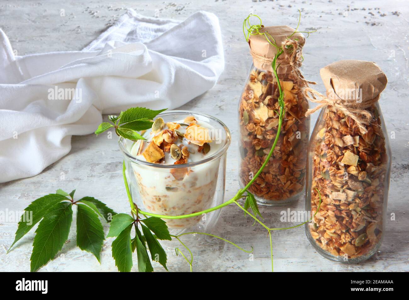 Müsli mit Joghurt in klarem Glas auf hellem Hintergrund. Granola in einer Glasflasche. Gesunde kalorienarme Lebensmittel. Naturprodukt. Vegetarisches Essen. Stockfoto