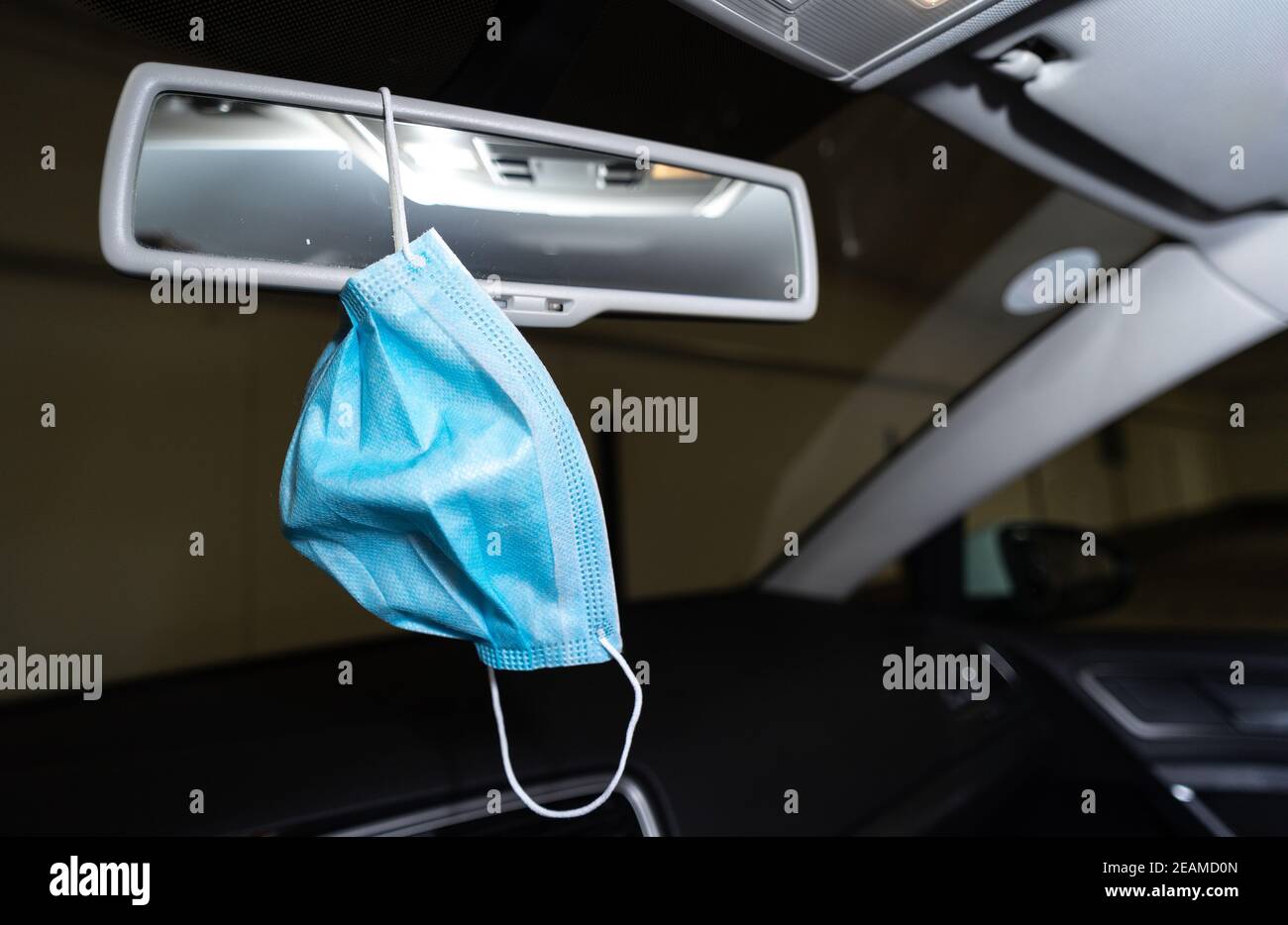 Medizinische Gesichtsmaske hängt auf dem Spiegel im Auto Stockfoto