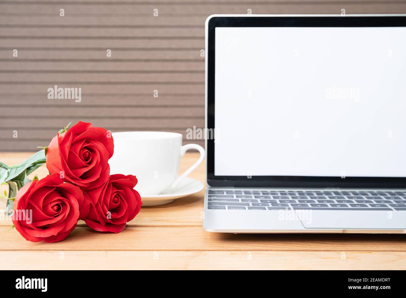 Rote Rose und Kaffeetasse mit Laptop-Mockup auf Holz Stockfoto