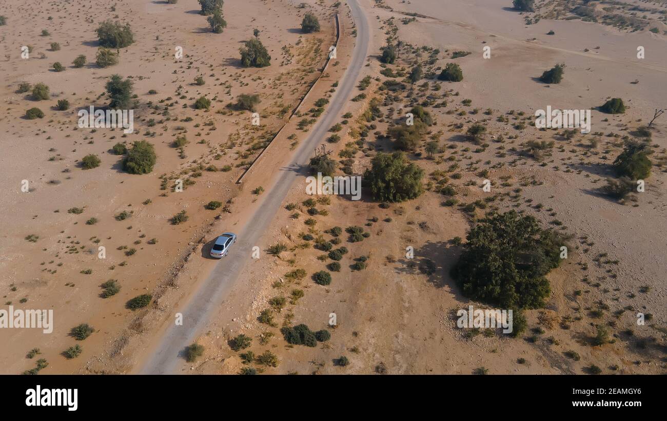 Luftaufnahme von silbernen Auto fahren auf Landstraße in der Wüste. Aufgenommen von Drohne, die über die Straße fliegt. Stockfoto