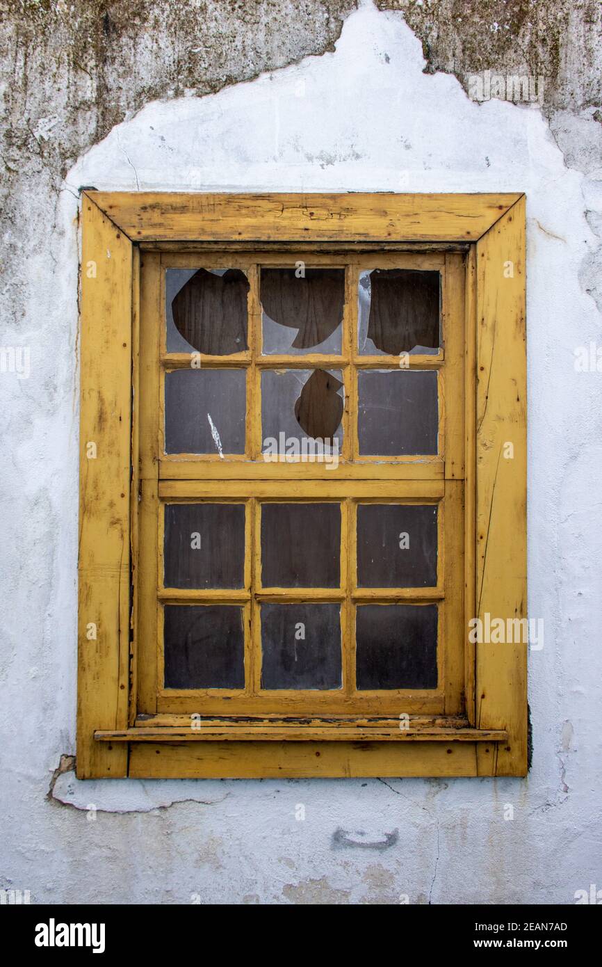 Zerstörtes altes gelbes Holzfenster mit kaputtem Glas und schmutzigen, beschädigten weißen Wänden. Detail Fenster in verlassenen ländlichen Haus. Vertikale Ausrichtung Stockfoto