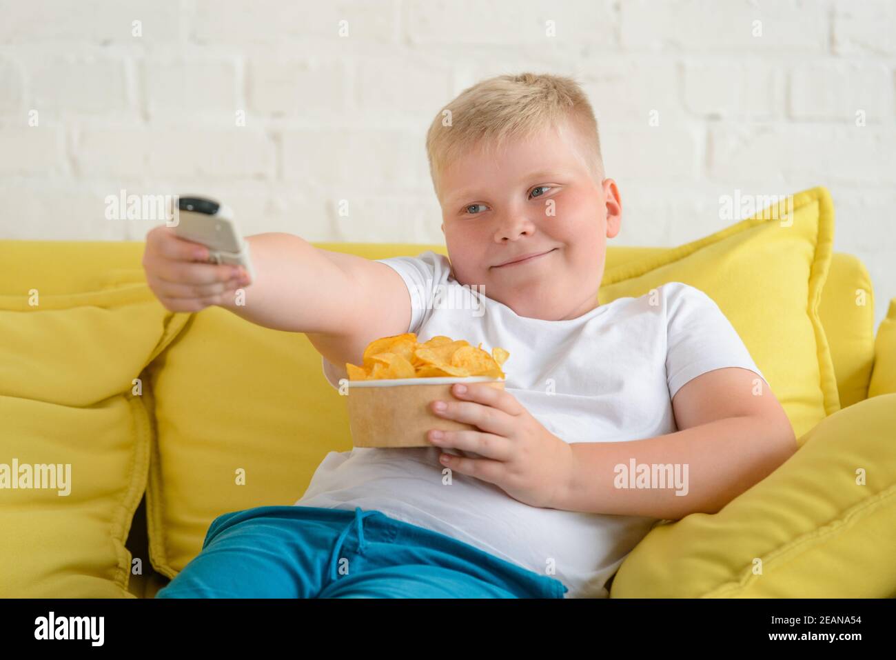 Übergewichtiger Junge, der Chips isst. Auf einem Sofa ruhen und den Fernseher einschalten Stockfoto