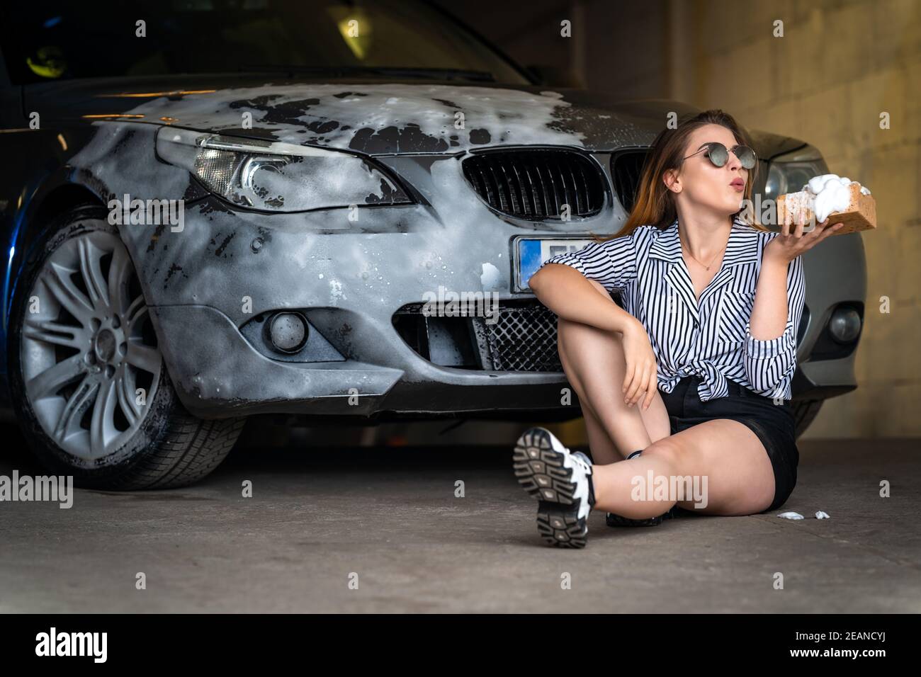 Eine junge attraktive Frau wäscht ein Auto mit einem Schwamm Und Schaum Stockfoto