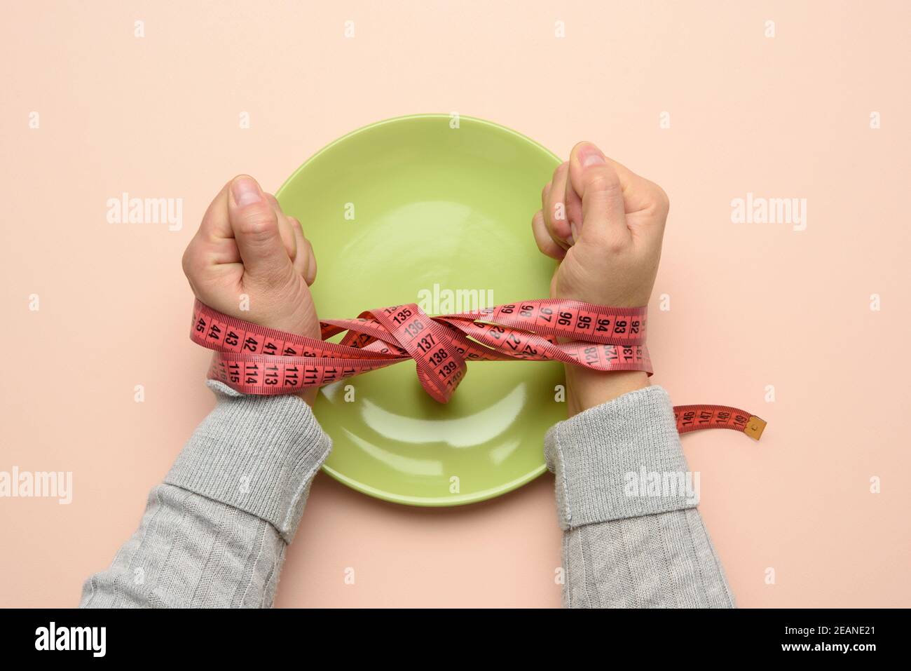 Zwei weibliche Hände gebunden mit grünem Maßband auf einem Grüne runde Keramikplatte Stockfoto
