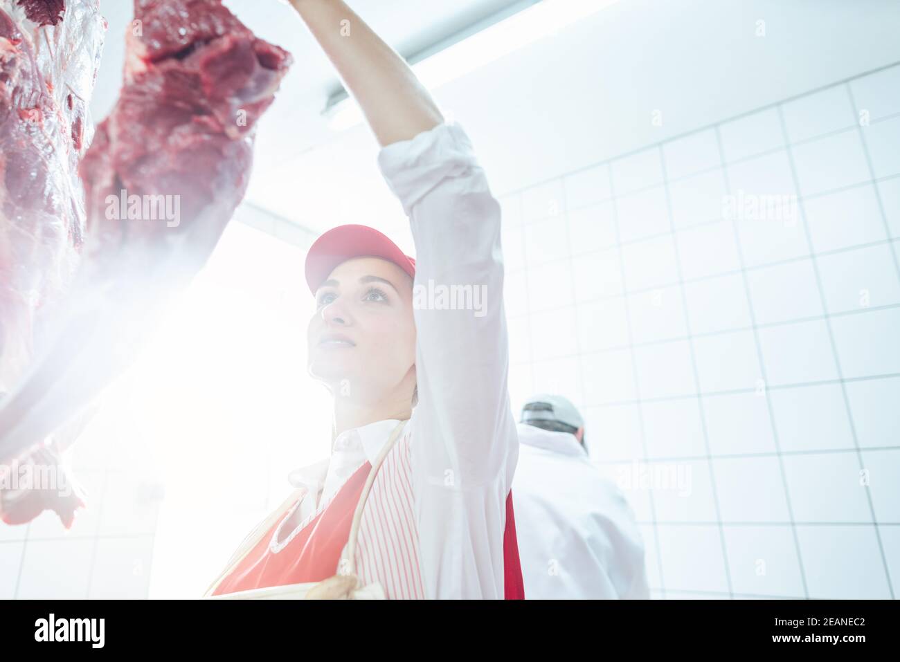 Metzgerfrau nimmt Fleisch vom Haken, um es zu schneiden und zu verkaufen Stockfoto