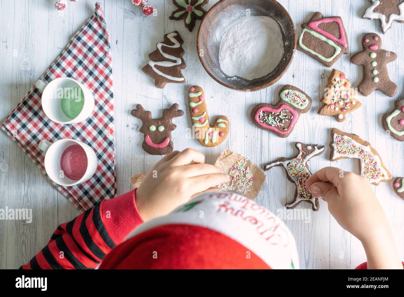 Niedliches kleines Kind mit Weihnachtsmütze schmückt die hausgemachten Lebkuchen zu Weihnachten von oben gesehen, Italien, Europa Stockfoto