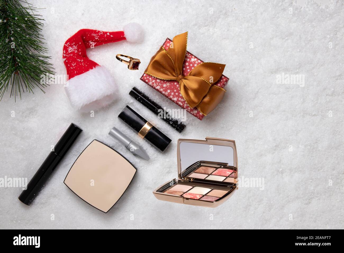Vorlage für weihnachtsverkauf. Draufsicht auf verschiedene Kosmetikprodukte und Beauty-Accessoires, ein Geschenk, einen Weihnachtsmütze und einen Tannenzweig auf weißem Schnee. Platz für Design. Stockfoto
