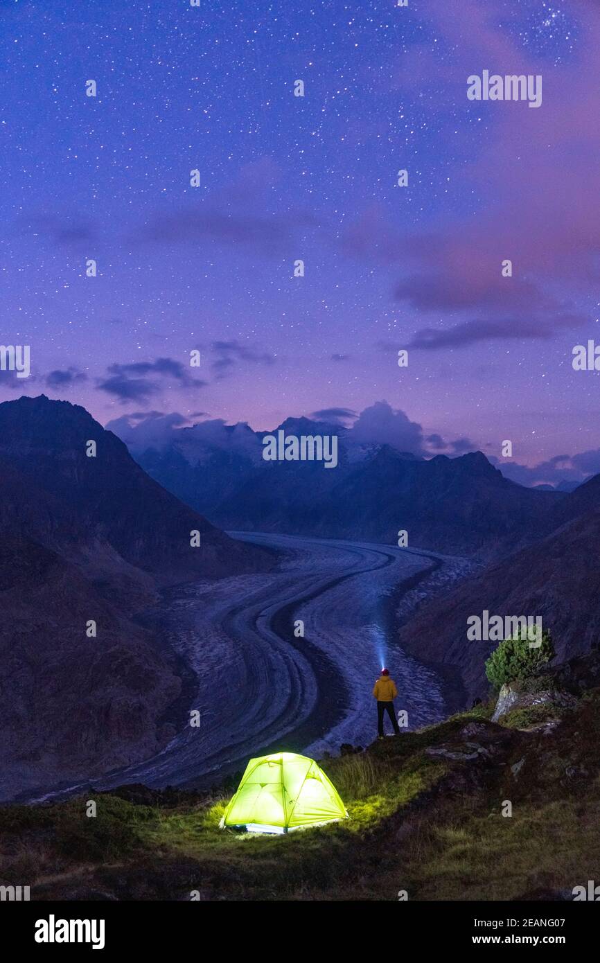 Wandermann mit Stirnlampe beleuchtet den Sternenhimmel in der Nähe des Zeltes am Aletschgletscher, Berner Alpen, Kanton Wallis, Schweiz, Europa Stockfoto