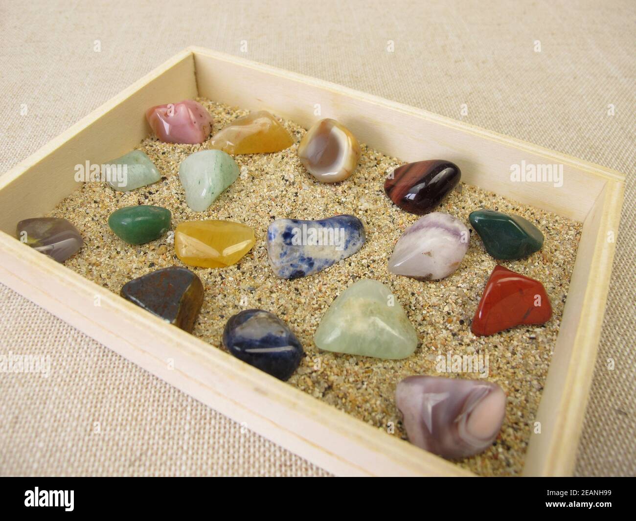 Getauchte Edelsteine in einer Holzkiste mit Sand Stockfoto