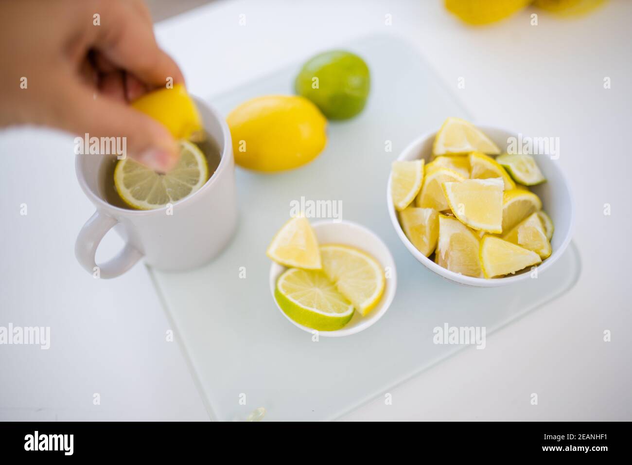 Weibliche Hand quetscht Zitrone in eine Tasse Zitronentee Stockfoto