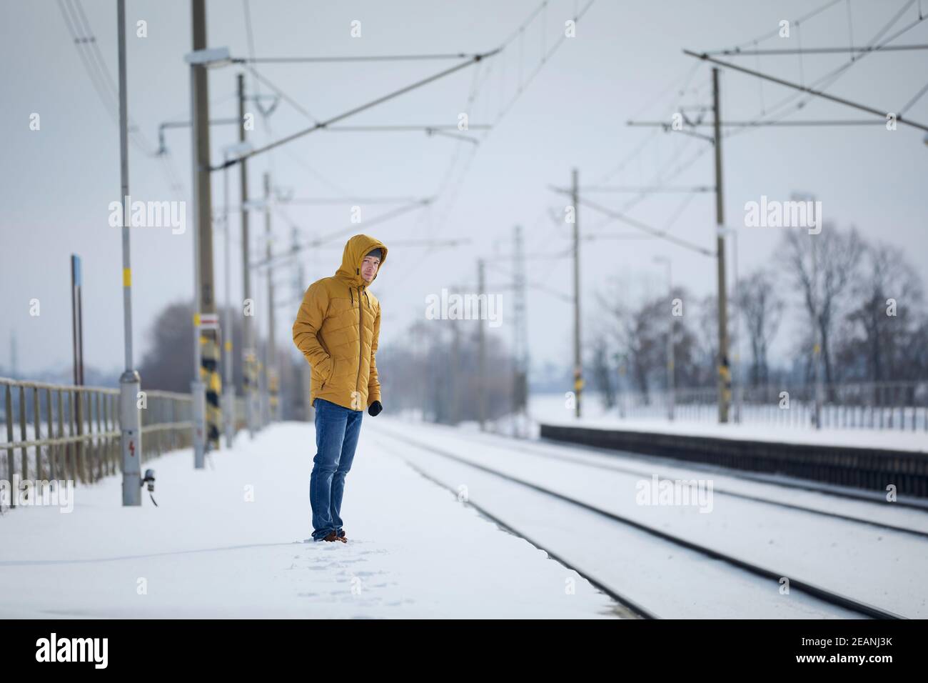 Verschneite Bahnhof während frostigen Tag. Mann, der auf dem Bahnsteig steht und auf einen verspäteten Zug wartet. Stockfoto