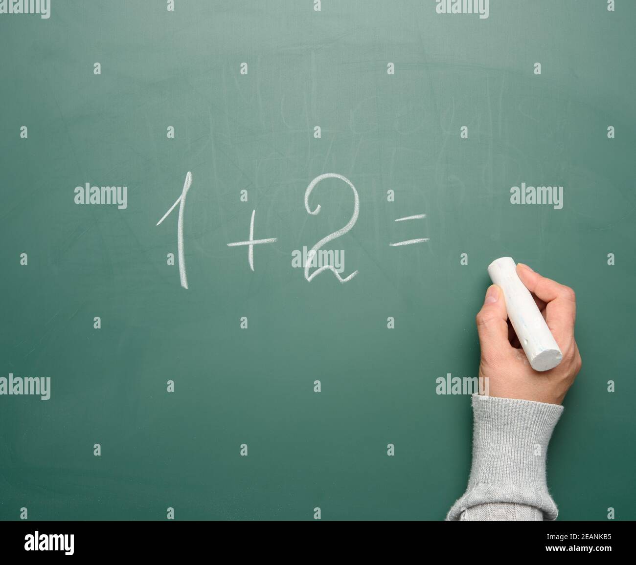 Mathe Beispiel in weißer Kreide auf grüner Kreide geschrieben Brett und eine Frauenhand mit weißer Kreide Stockfoto