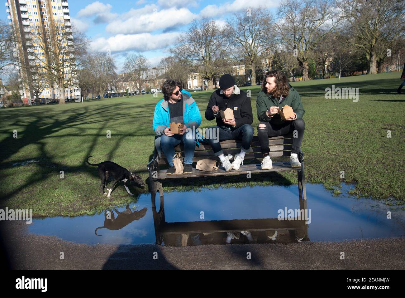 London, Hackney. London Fields. Drei Freunde essen im Park zu Mittag und halten ihre Füße trocken. Stockfoto