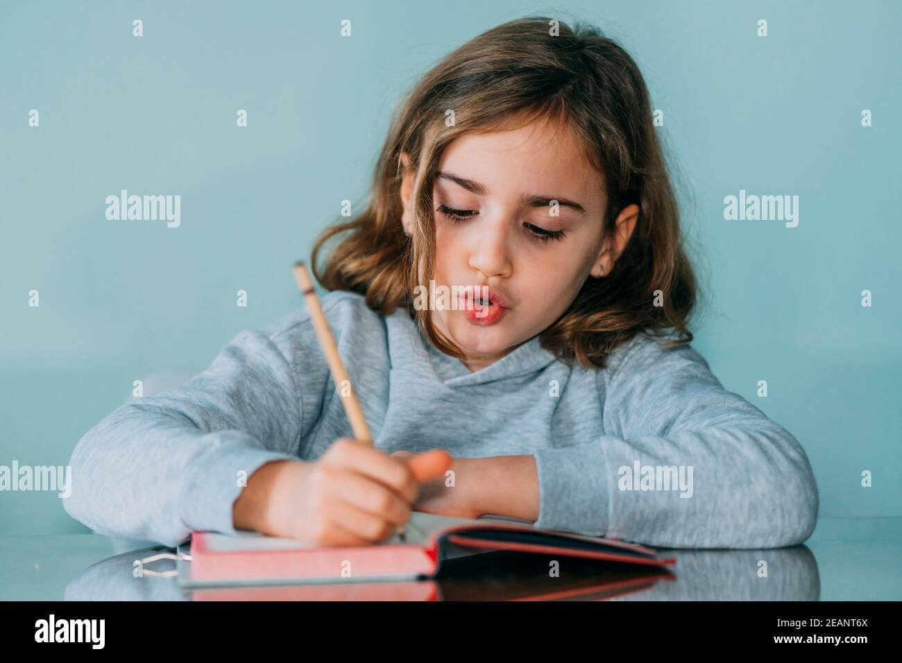 Liebenswert kleines Mädchen schreibt in einem Notizbuch, hat eine nachdenkliche und lustige Geste. Horizontales Foto Stockfoto