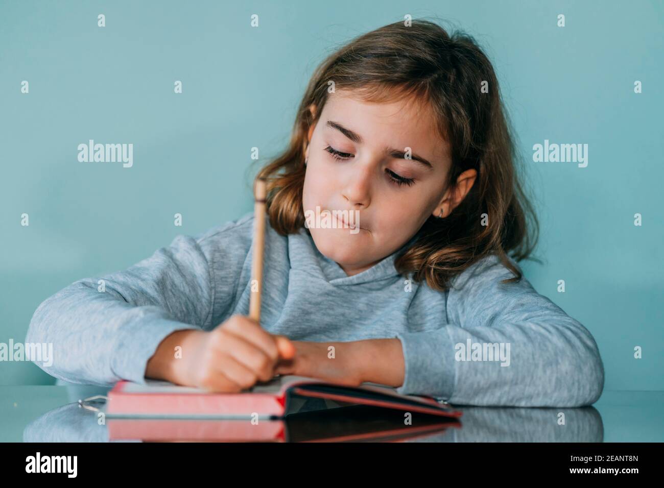 Liebenswert kleines Mädchen schreibt in einem Notizbuch, hat eine nachdenkliche und lustige Geste. Horizontales Foto Stockfoto