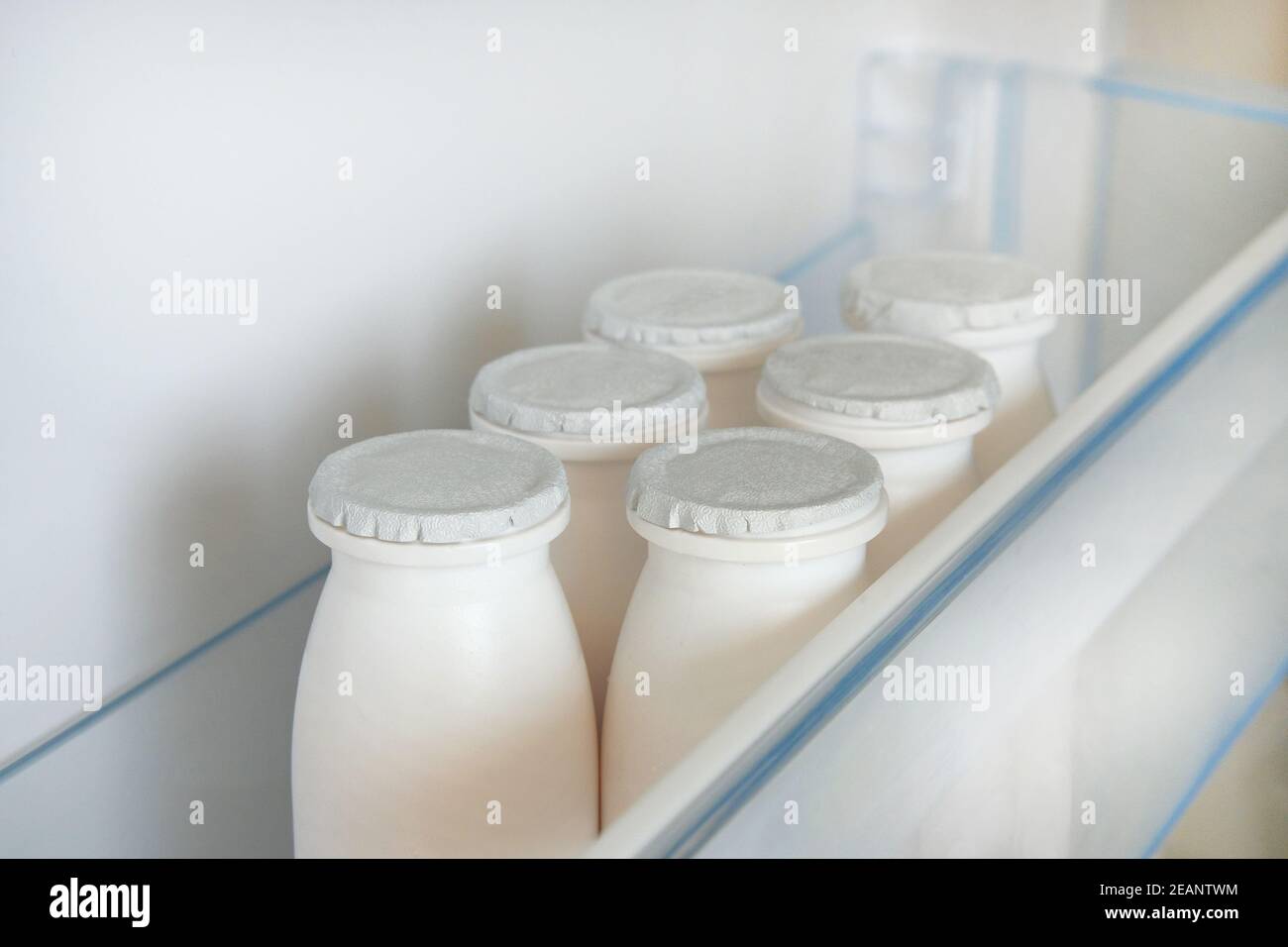 Weiße Flaschen von Kefir im Regal von offenen leeren Kühlschrank. Fermentiertes Lebensmittelkonzept. Stockfoto