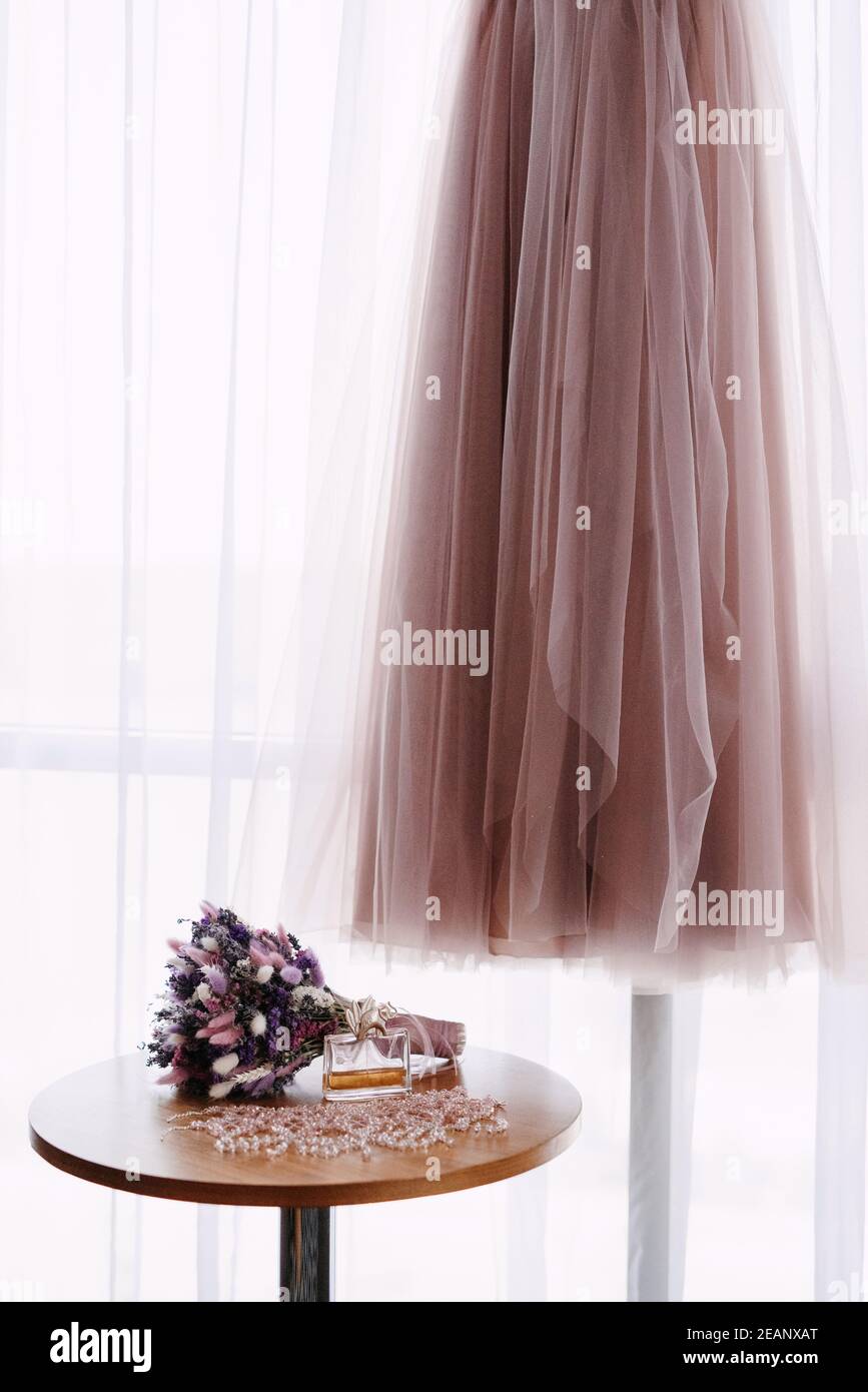 Rosa Hochzeitskleid auf dem Hintergrund des Fensters mit Der Brautstrauß Stockfoto