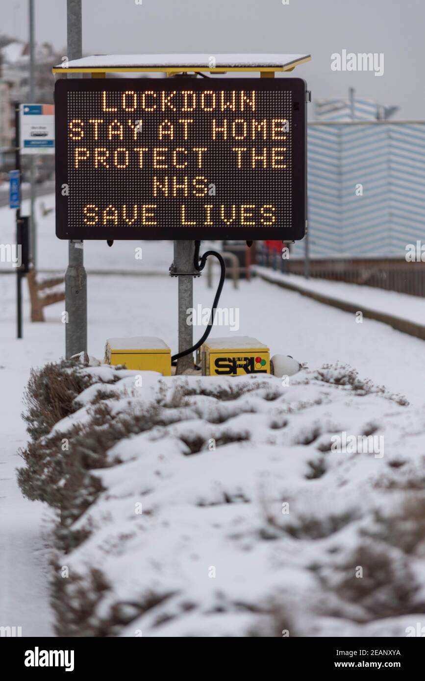 Matrixzeichen Warnung vor COVID 19 Lockdown Maßnahmen in Southend on Sea, Essex, UK, mit Schnee von Storm Darcy. Bleib zu Hause, schütze den NHS-Slogan Stockfoto