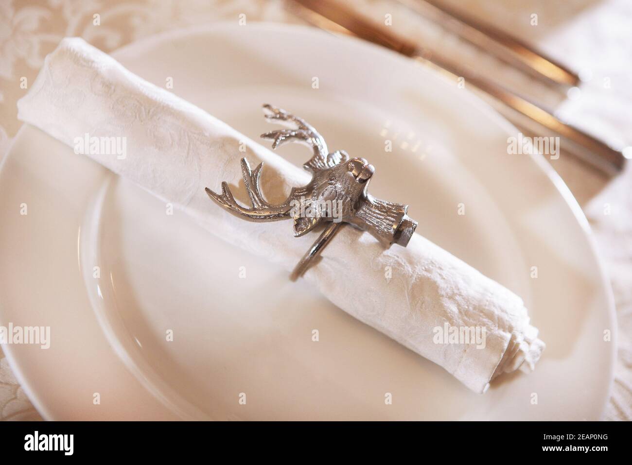 Die weiße Stoffserviette wird mit einem Ring in Form eines Hirschkopfes gesichert. Der Blick von oben. Makrofoto. Speicherplatz kopieren. Stockfoto
