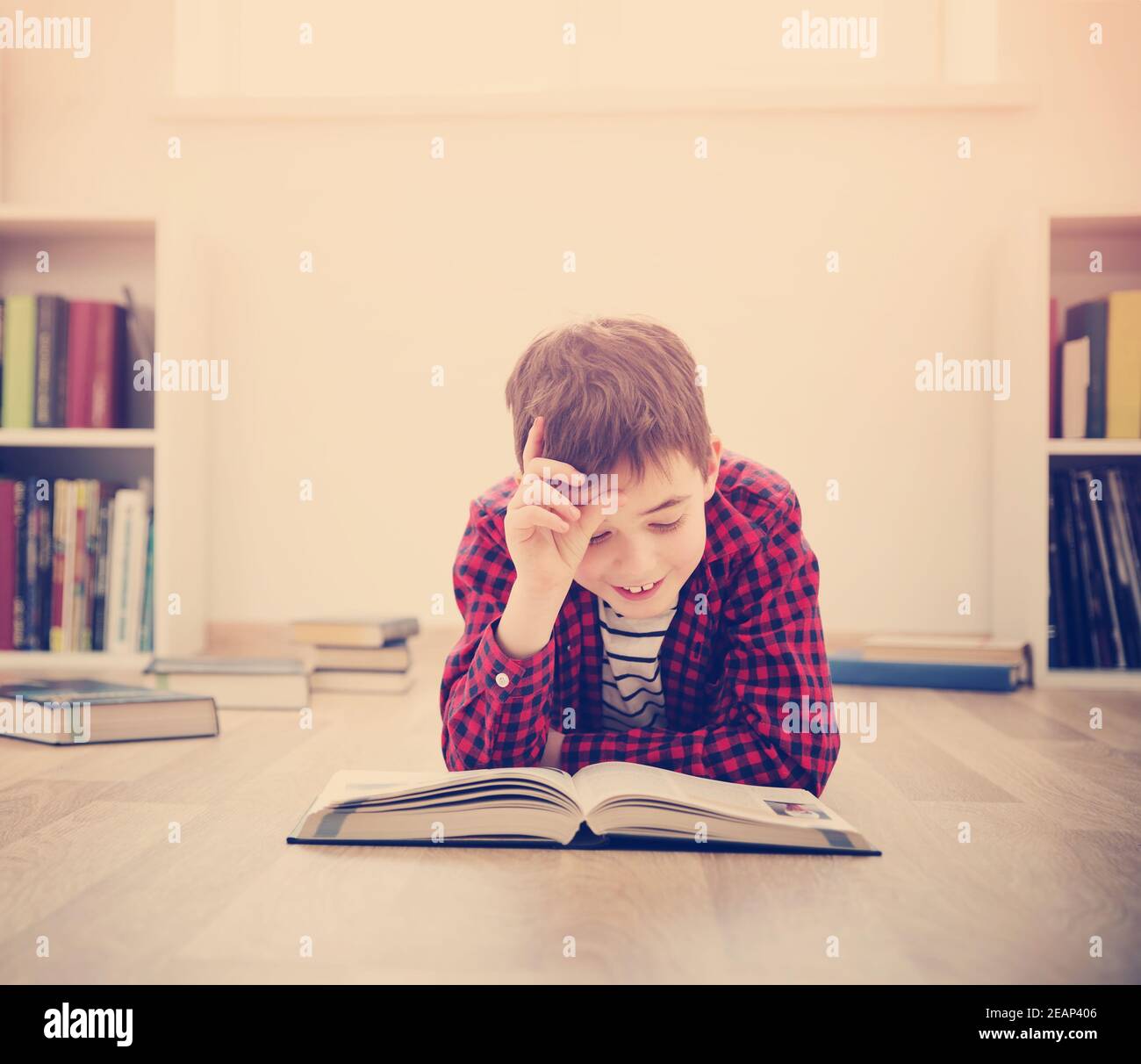 Acht Jahre altes Kind auf dem Boden liegend unter Bücher zu Hause Stockfoto
