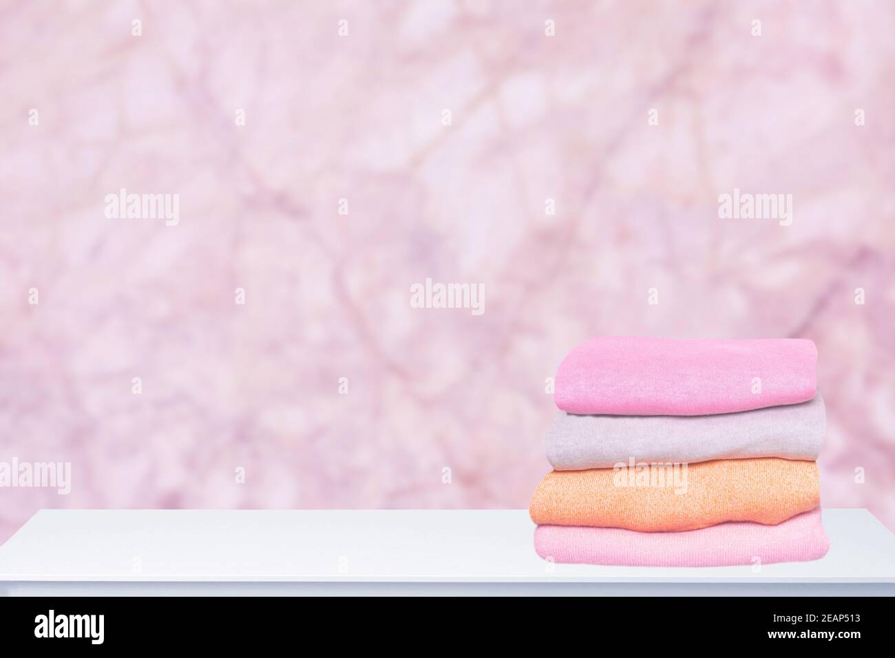 Ein Stapel von bunten, warmen Pullovern auf einem hellen Tisch vor abstraktem, unscharfem rosa Hintergrund. Herbst- und Frühlingskleidung. Platz für die Montage der Produktanzeige. Stockfoto