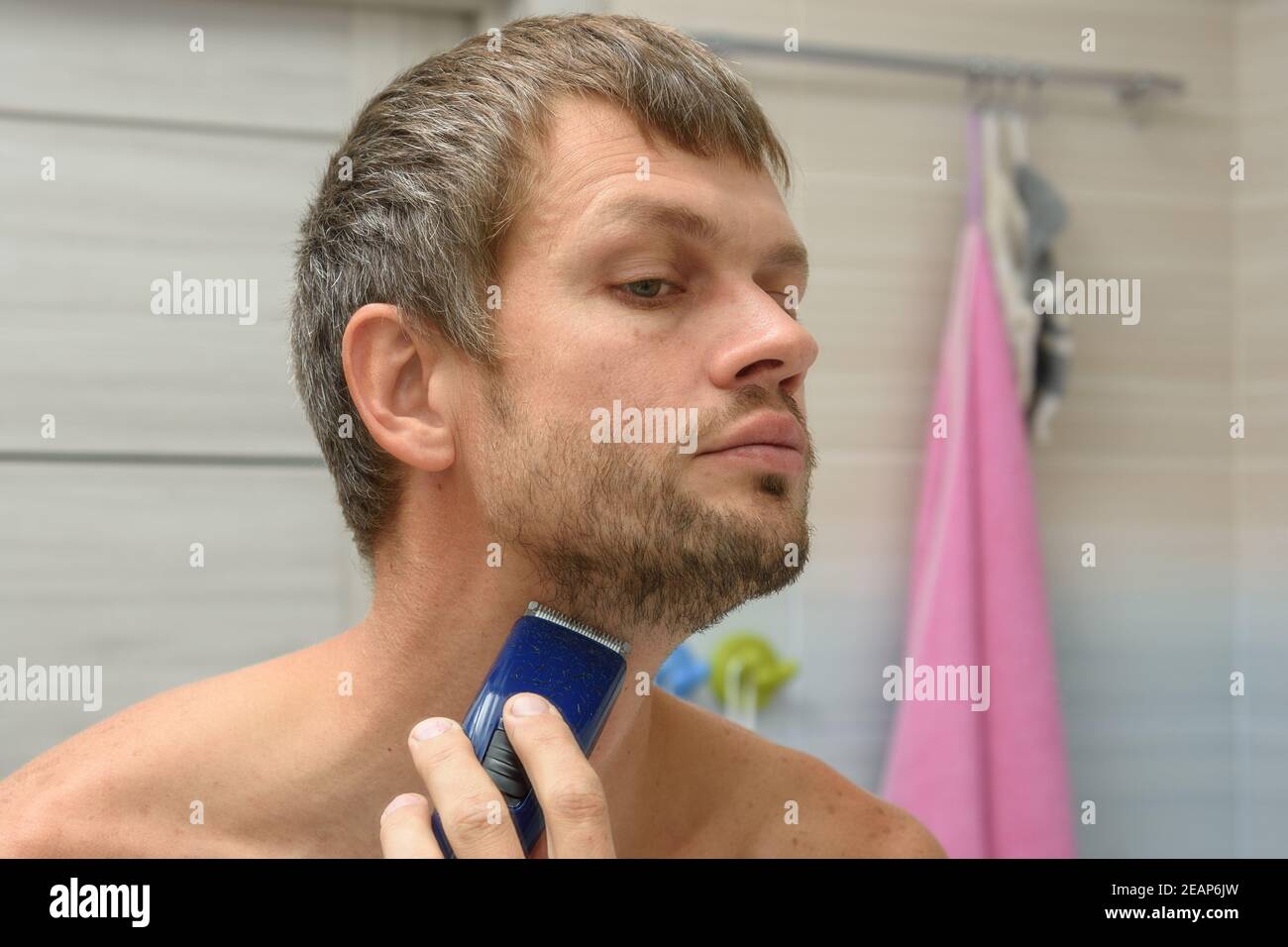Ein Mann glättet seinen Bart auf seinem Gesicht mit einem Haarschneider Stockfoto