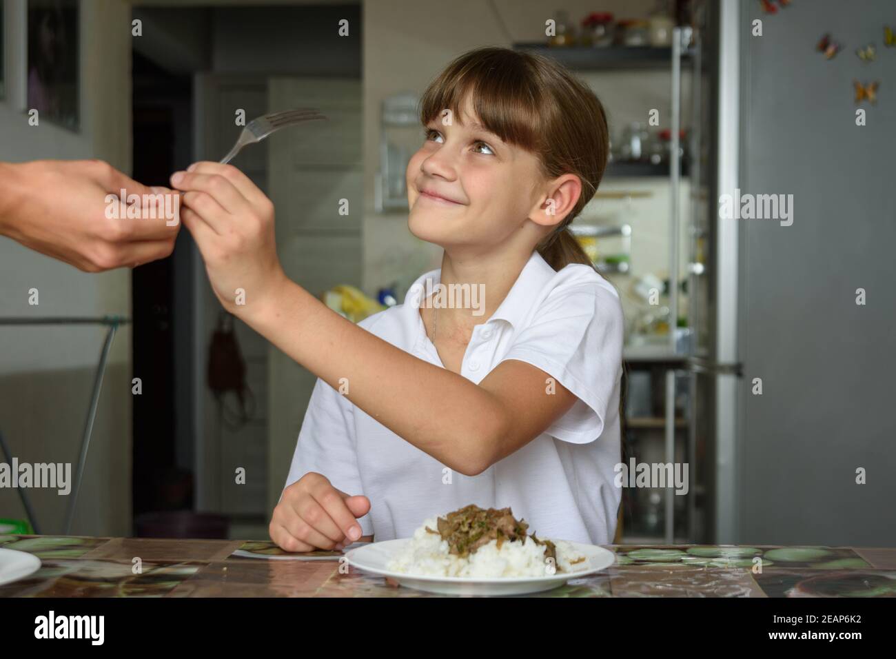 Ein Mädchen nimmt der Mutter eine Gabel aus der Hand Vorbereitung auf das Essen am Küchentisch Stockfoto