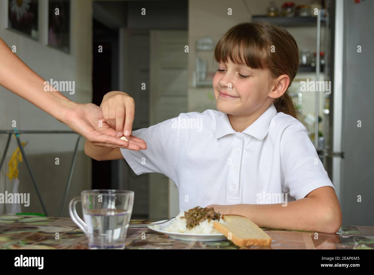 Ein Mädchen nimmt ihrer Mutter schon einmal Medikamente aus der Hand Abendessen Stockfoto