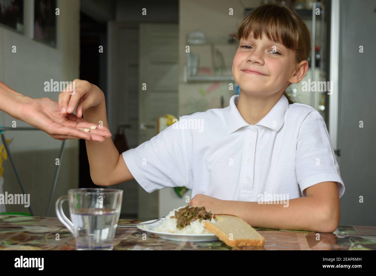 Mamas Hand hält zwei Pillen an das Mädchen Vor dem Mittagessen einnehmen Stockfoto