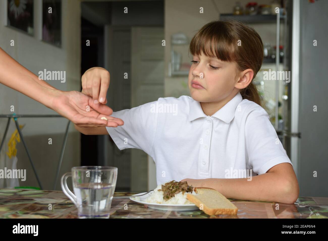 Einem kranken Mädchen vor dem Essen hält Mutter Medizin in ihrer Handfläche Stockfoto